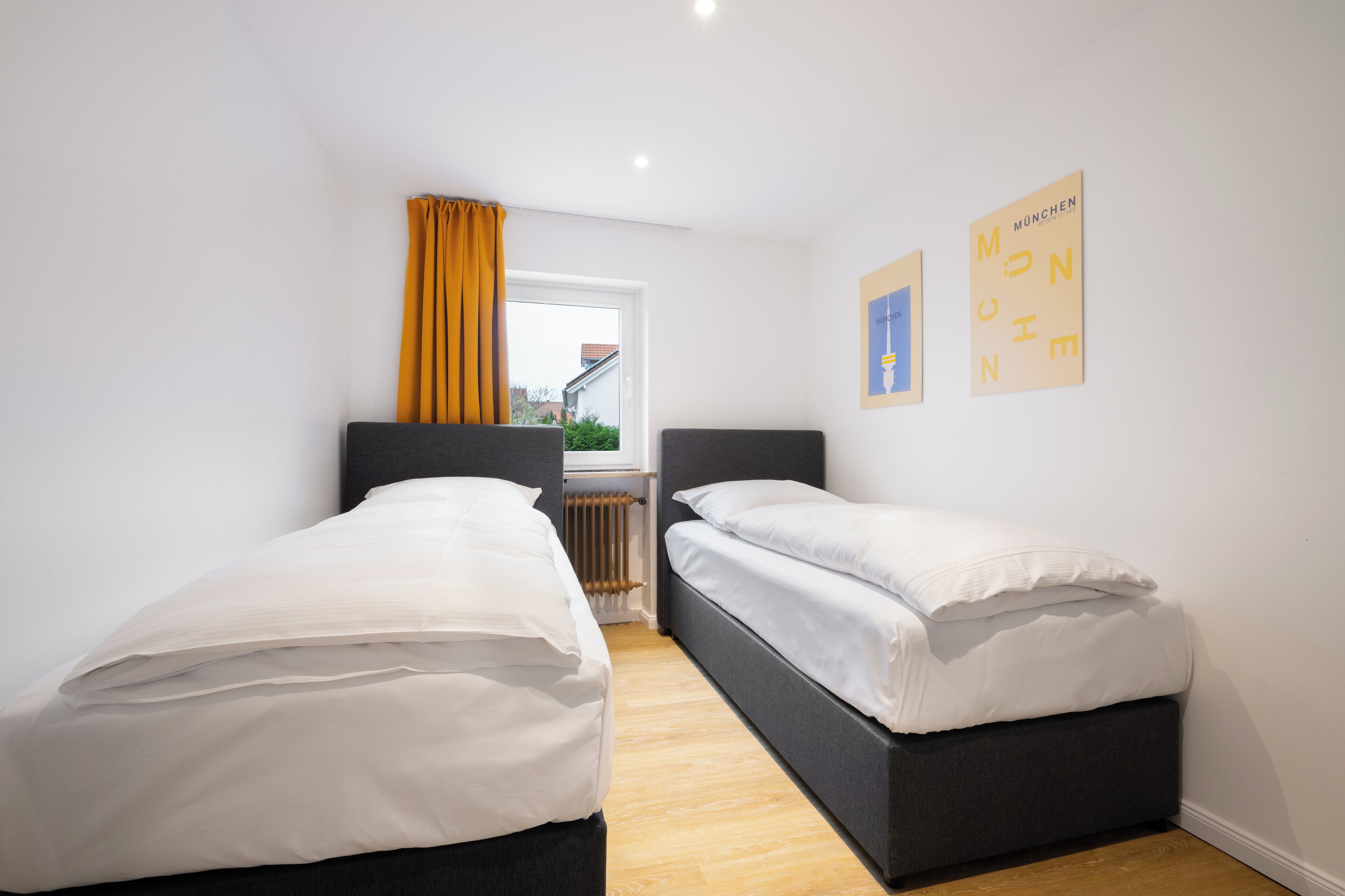 A bedroom with two single beds, a window with yellow curtains, and a radiator.
