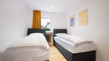 A bedroom with two single beds, a window with yellow curtains, and a radiator.