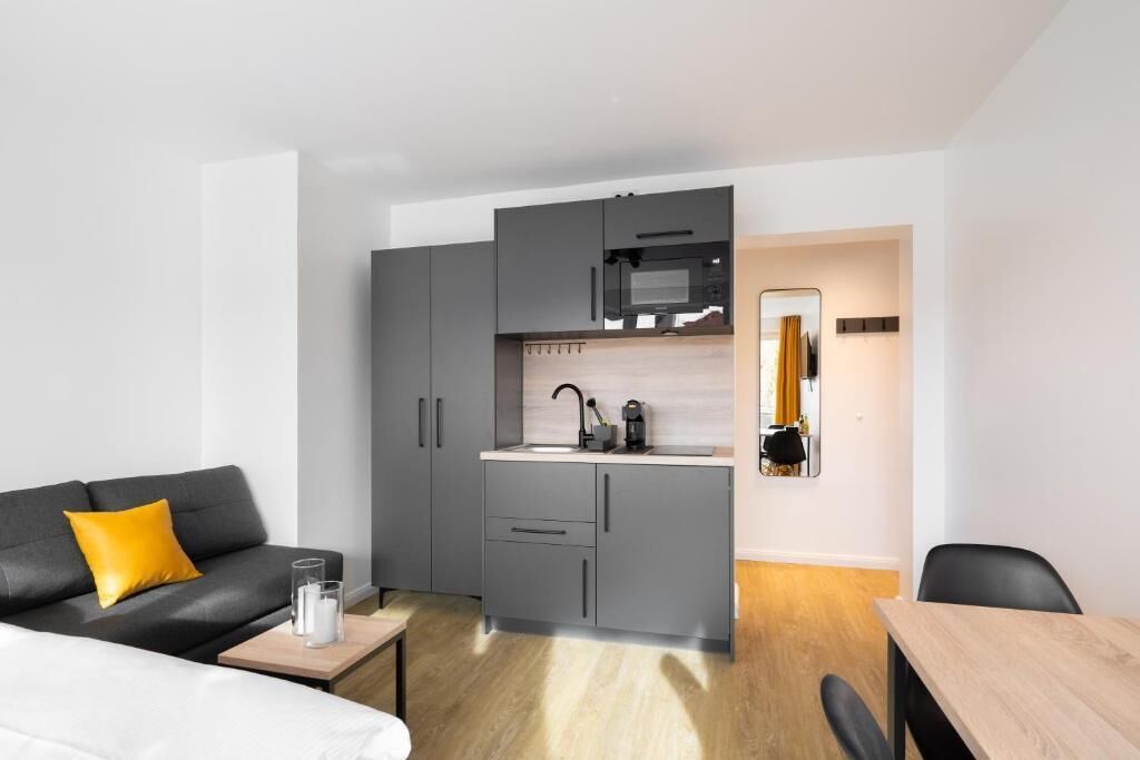 A compact living space with a kitchenette, a sofa with a yellow cushion, a small table, and a mirror.