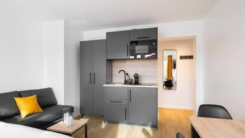 A compact living space with a kitchenette, a sofa with a yellow cushion, a small table, and a mirror.