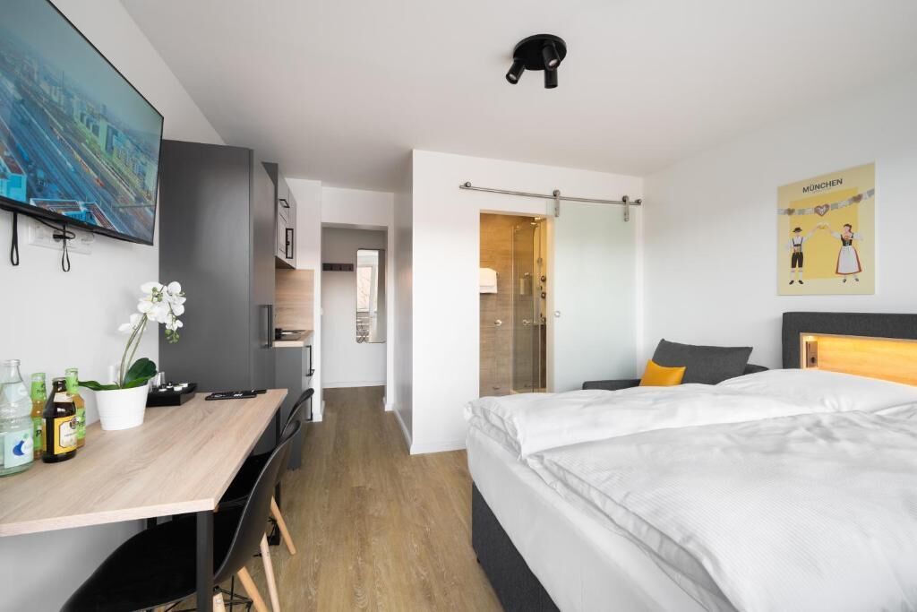 A modern hotel room with a bed, desk, and shower area.