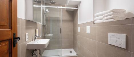Un baño moderno con ducha de vidrio, lavamanos y una pila de toallas blancas en la pared.
