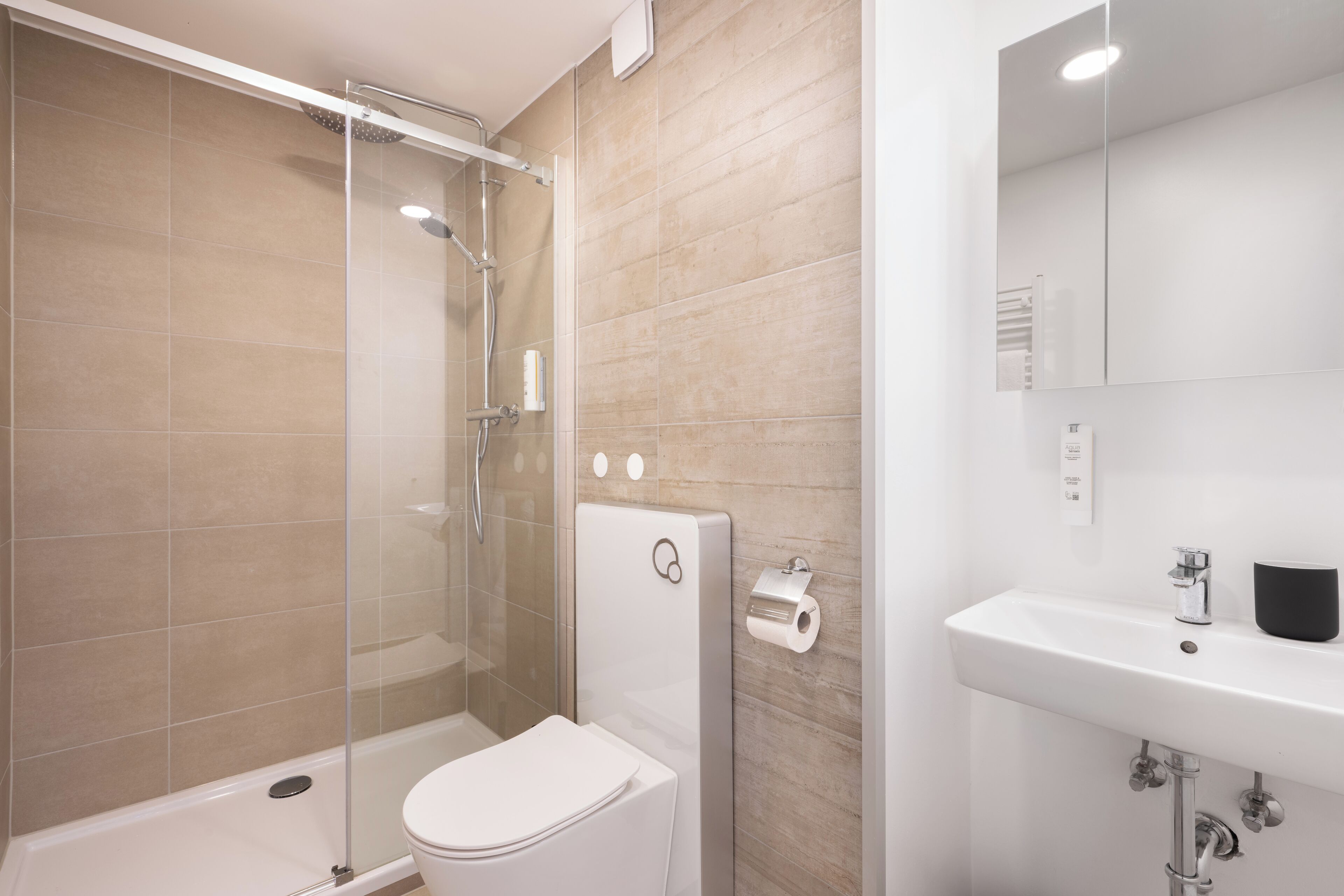 Une salle de bain moderne avec une douche à parois de verre, des toilettes blanches et un lavabo avec un miroir.