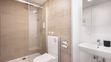 Une salle de bain moderne avec une douche à parois de verre, des toilettes blanches et un lavabo avec un miroir.