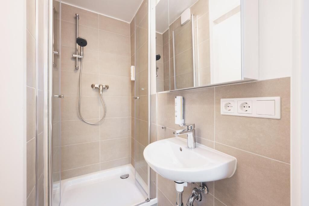 Une salle de bain moderne avec une douche à parois de verre, un lavabo blanc et un miroir.