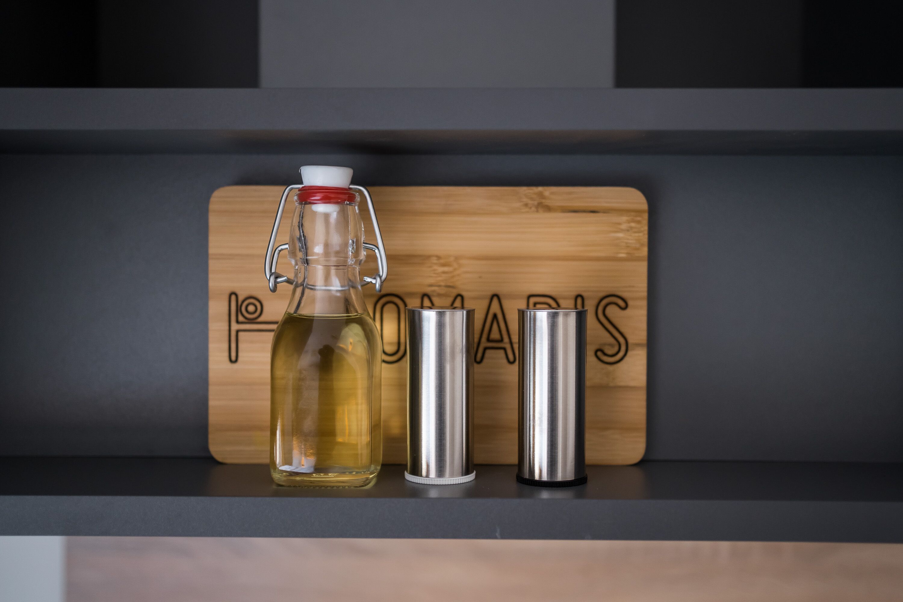 A wooden board with the word "POMARIS" on it, a glass bottle with a metal cap, and two metal containers on a shelf.