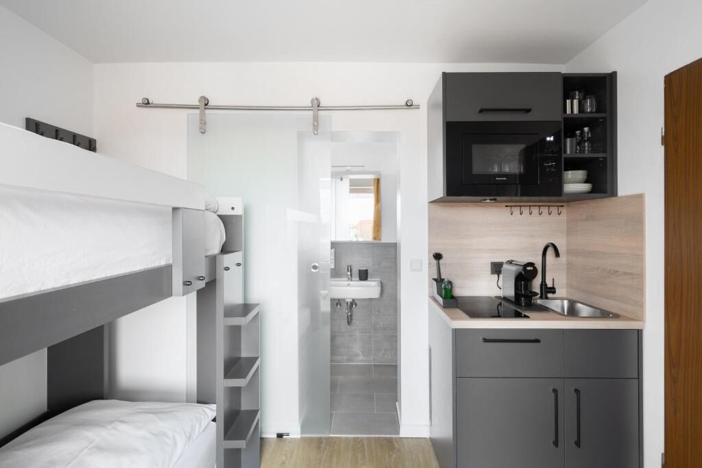 A compact hotel room with a bunk bed, a kitchenette with a microwave and coffee maker, and a small bathroom with a sink.