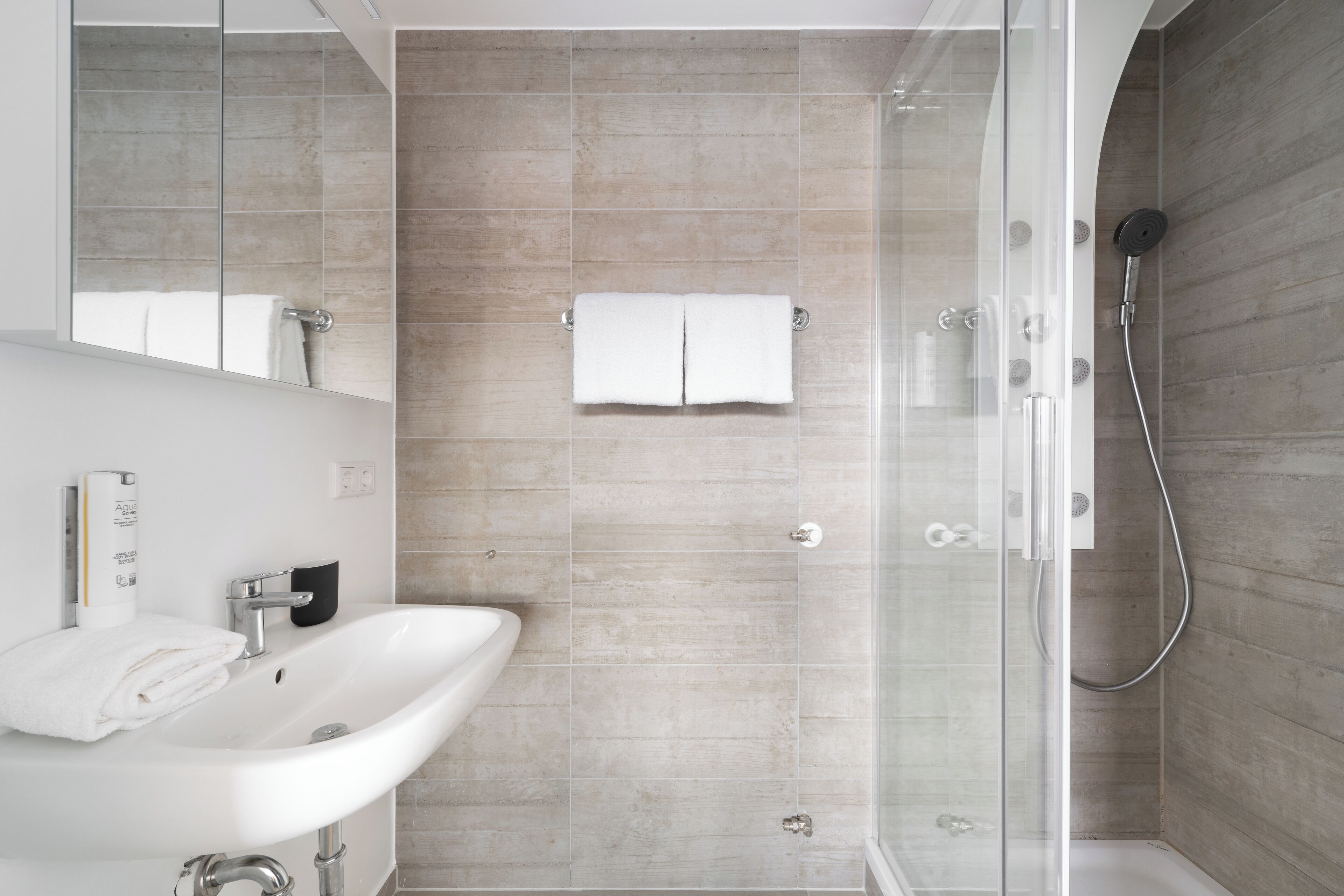 A modern bathroom with a glass shower enclosure, a white sink, and a towel rack.