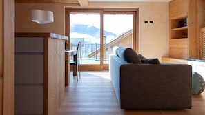A modern living room with a sofa, a dining table, and a view of mountains through large glass doors. - Sertorelli 27 (Bormio)