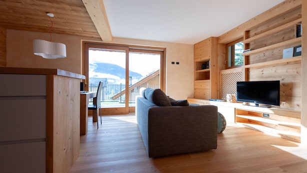 Ein modernes Holzinterieur mit einer Couch, einem Fernseher und einem Essbereich mit Blick auf die Berge.