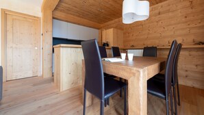 Ein Esszimmer mit Holzboden, einem Tisch und Stühlen, einer Küche im Hintergrund und einer Holzzieldecke.