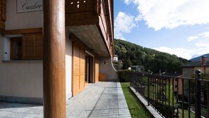 Ein Gebäude mit Holztüren und einem Steinweg, der zu einem umzäunten Bereich mit Bergblick führt.