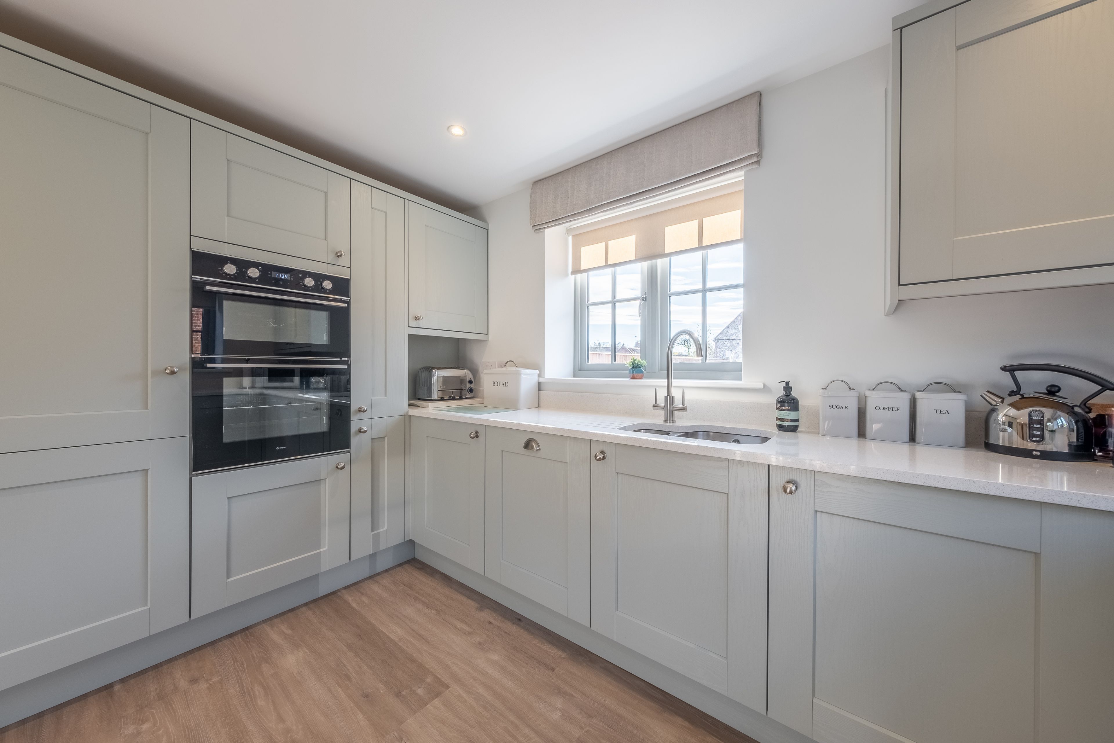 A modern kitchen with white cabinets, a built-in oven, a sink, and a window with a view.