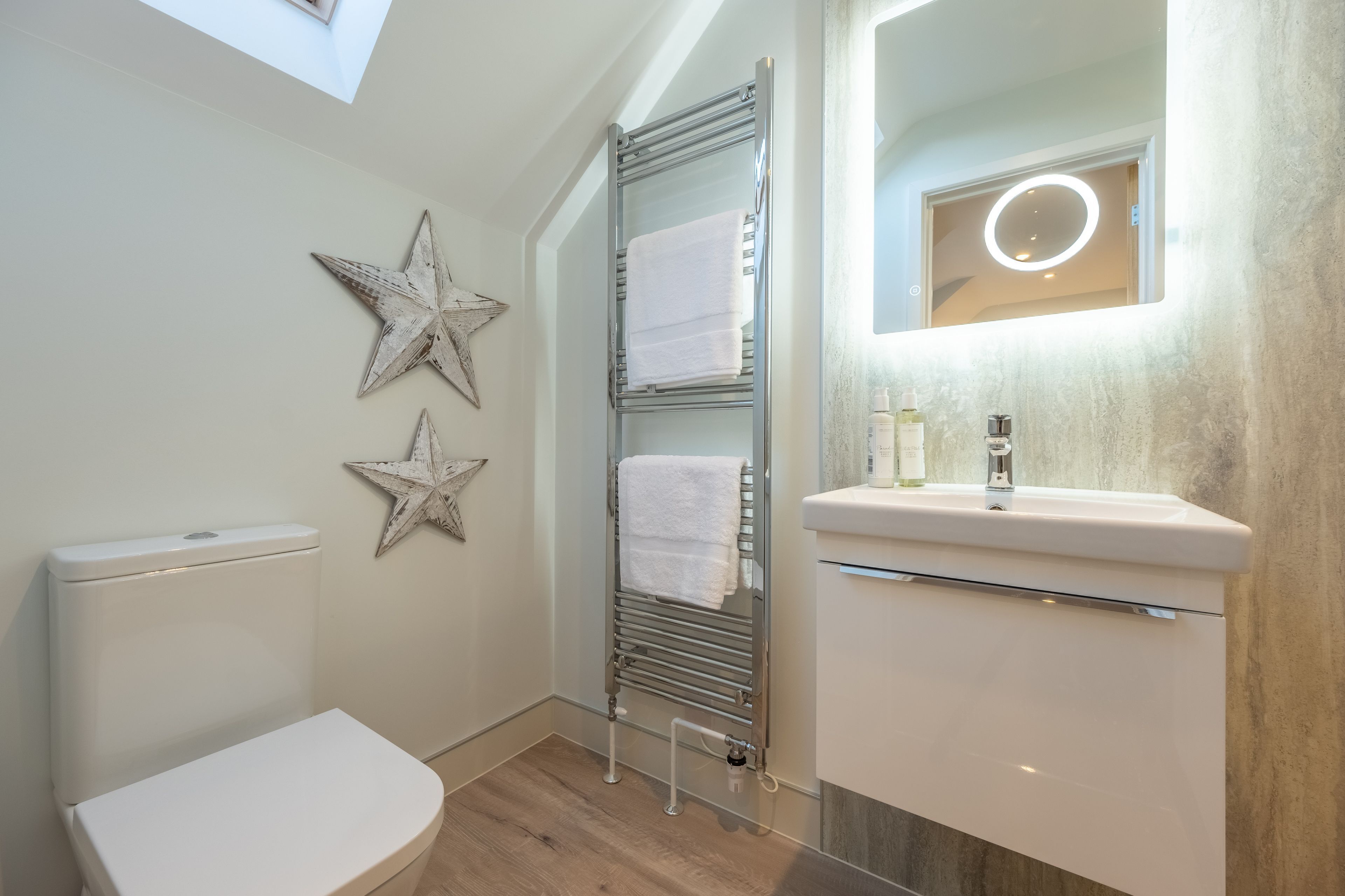 Un baño con inodoro, un perchero con dos toallas, un lavamanos y un espejo, además de decoración de pared con estrellas.