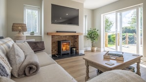 A living room with a fireplace, a sofa, a coffee table, and a TV mounted on the wall. - Larks Rise, Burnham Market, Norfolk (Burnham Market)
