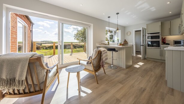 A modern kitchen with a large window, a dining area with a wooden table and chairs, and a view of the outdoors. - Larks Rise, Burnham Market, Norfolk (Burnham Market)