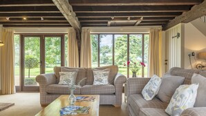 A cozy living room with two sofas, a coffee table, and large windows offering a view of greenery. - The Granary, Oulton, Norfolk (Oulton)