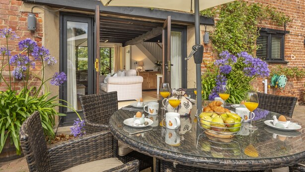 A breakfast table set with eggs, croissants, and fruit, a wicker chair, and a glass table. - The Granary, Oulton, Norfolk (Oulton)