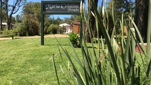 A sign reading "Maria Cristina Posada" in a garden setting with grass, trees, and a wooden structure in the background. - Posada María Cristina (Punta del Este)