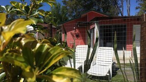 A red building with a fenced yard, two white chairs, and a small garden area. - Posada María Cristina (Punta del Este)