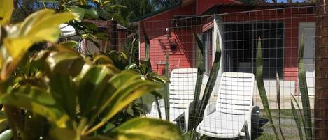 A red building with a fenced yard, two white chairs, and a small garden area.