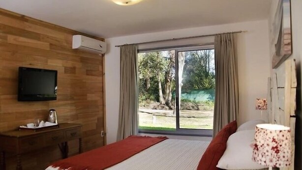 A hotel room with a bed, a desk with a television, and a window with curtains. - Posada María Cristina (Punta del Este)