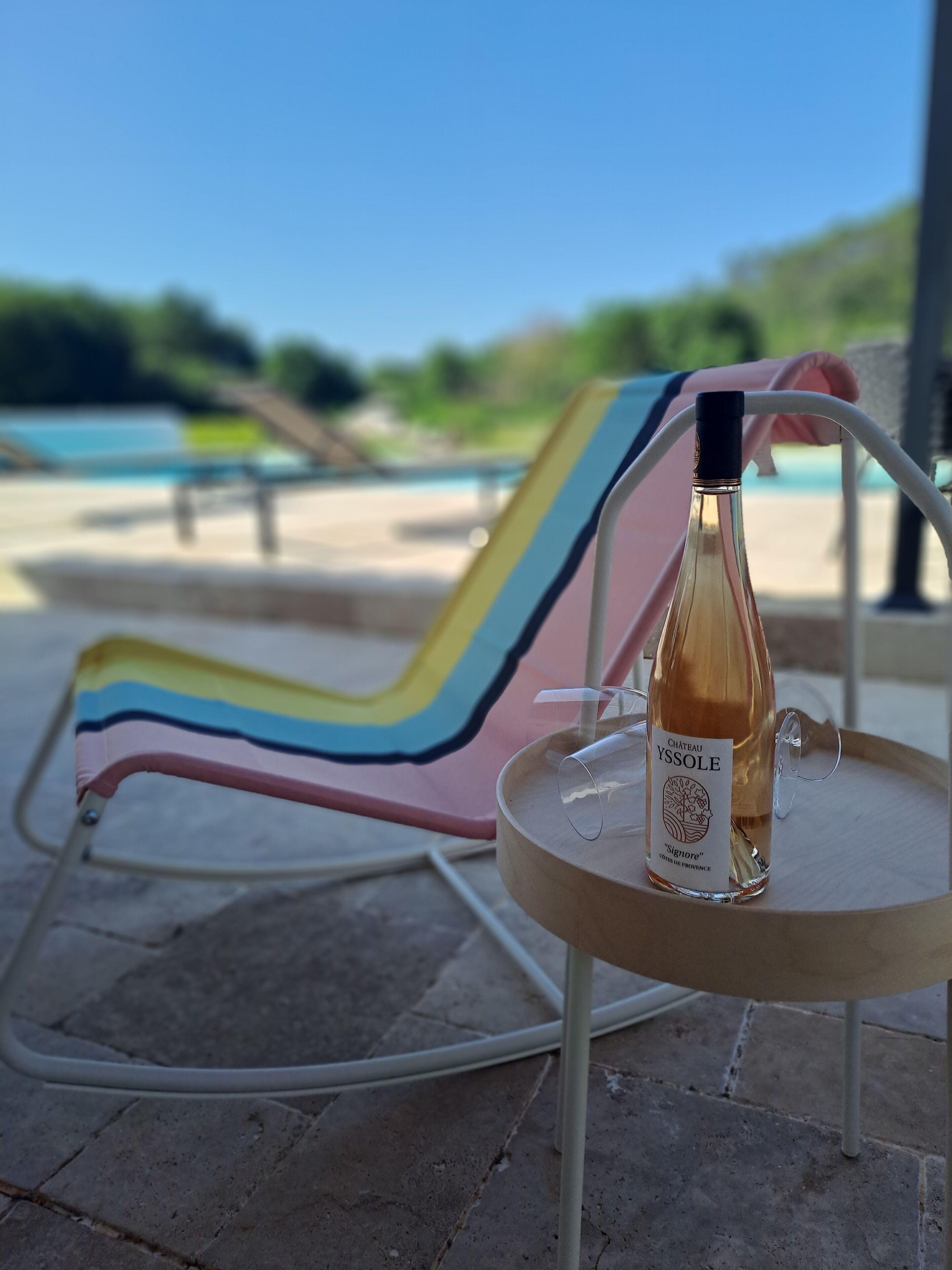 A bottle of Château Yssole wine on a small round table with a metal frame, placed on a tiled floor.
