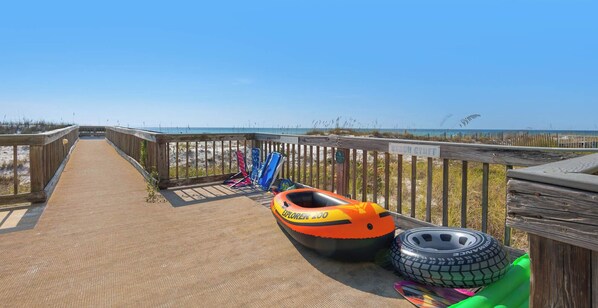 A wooden boardwalk leading to a beach with a kayak and a tire.