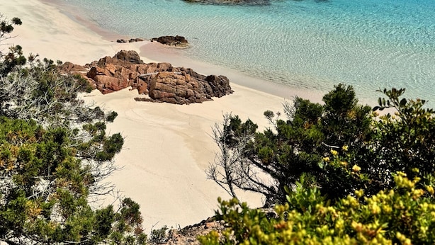 Ein Strand mit klarem türkisblauem Wasser, Felsformationen und Sandküste.