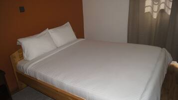 A single bed with white bedding in a room with an orange wall and a wooden floor.