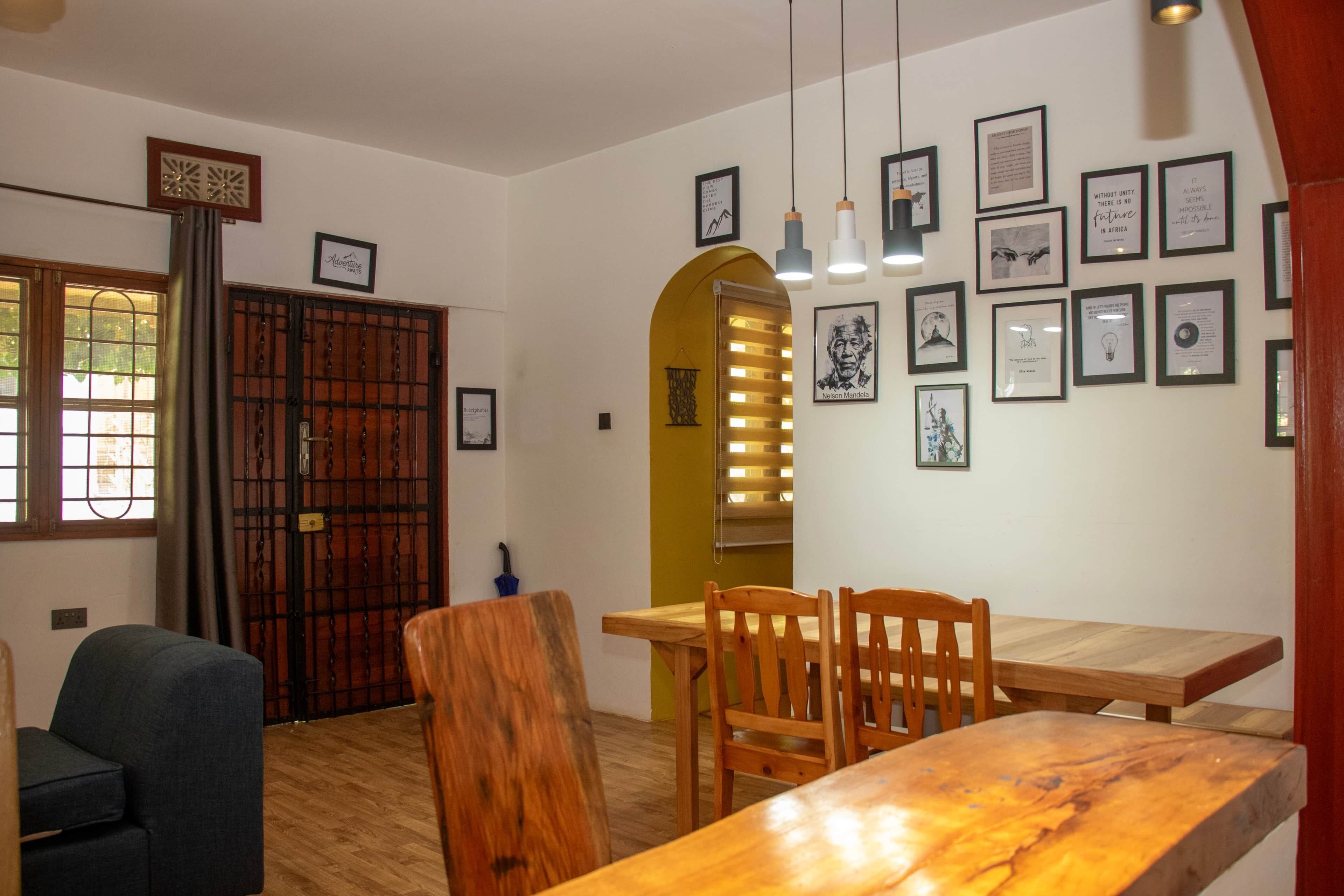 A dining area with a wooden table and chairs, a window with a view, and a wall decorated with framed pictures.
