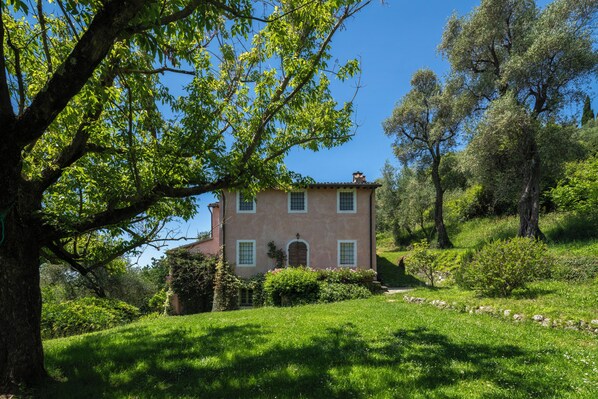 A two-story building with a garden in front, surrounded by trees.