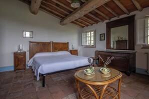 A bedroom with a bed, bedside tables, a dresser, a mirror, and a round table with a vase.