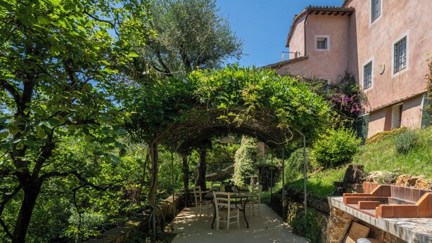 A garden with a pergola, outdoor seating, and a building in the background.