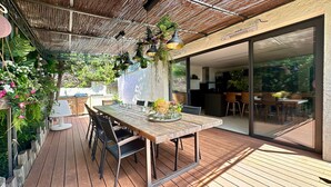 An outdoor dining area with a wooden table, chairs, hanging plants, and a pergola. - - (Cannes)
