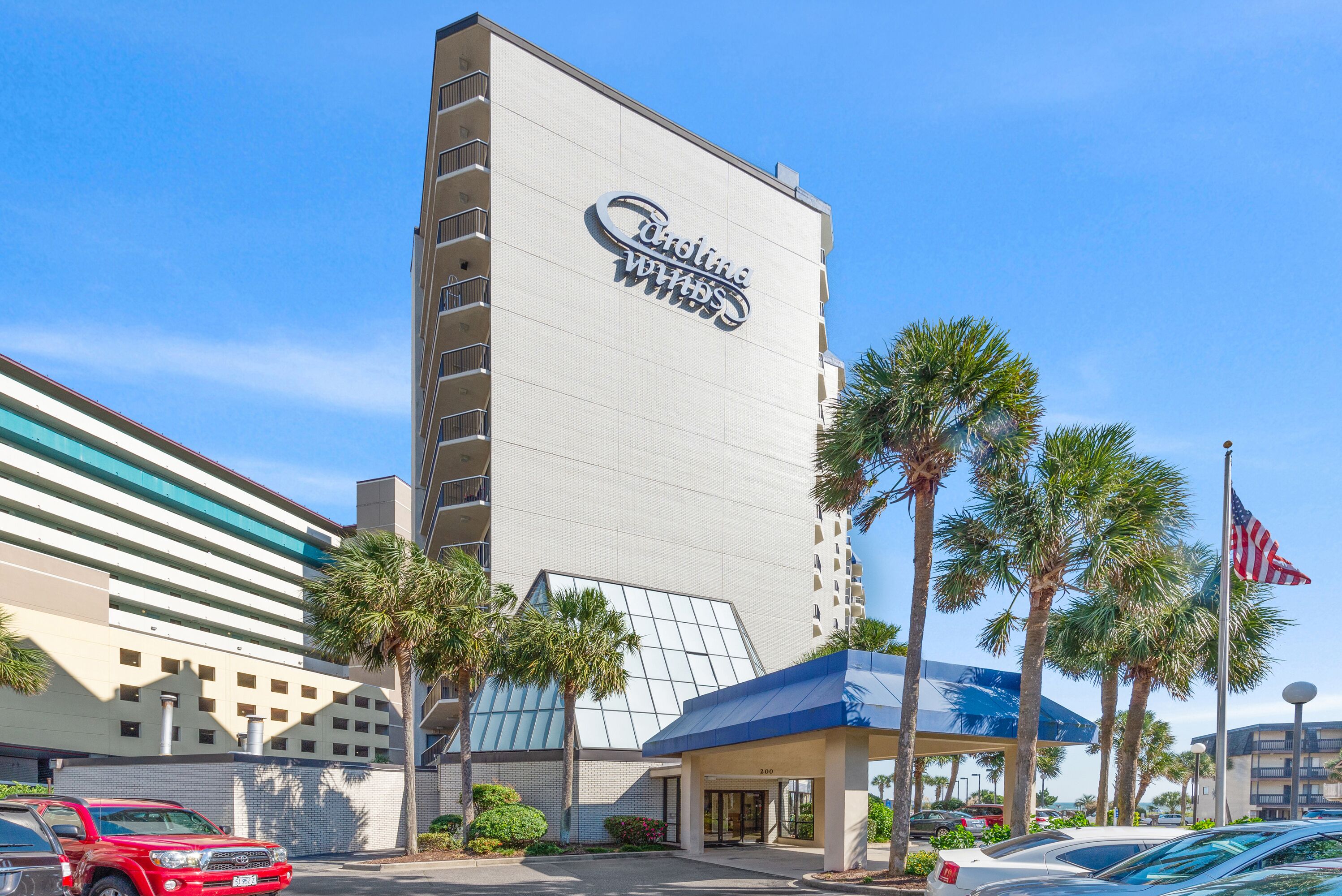 A hotel with a prominent sign, a covered entrance, and palm trees.