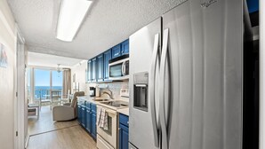 A modern kitchen with stainless steel appliances, blue cabinets, and a view to the outside.