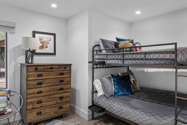 A bunk bed with a quilted gray mattress, a wooden dresser with multiple drawers, a framed deer artwork on the wall, and a floor lamp. - Mountain Blue Mesa Condo by InvitedHome | Ski-In/Ski-Out, Village Core, Walkable (Telluride)