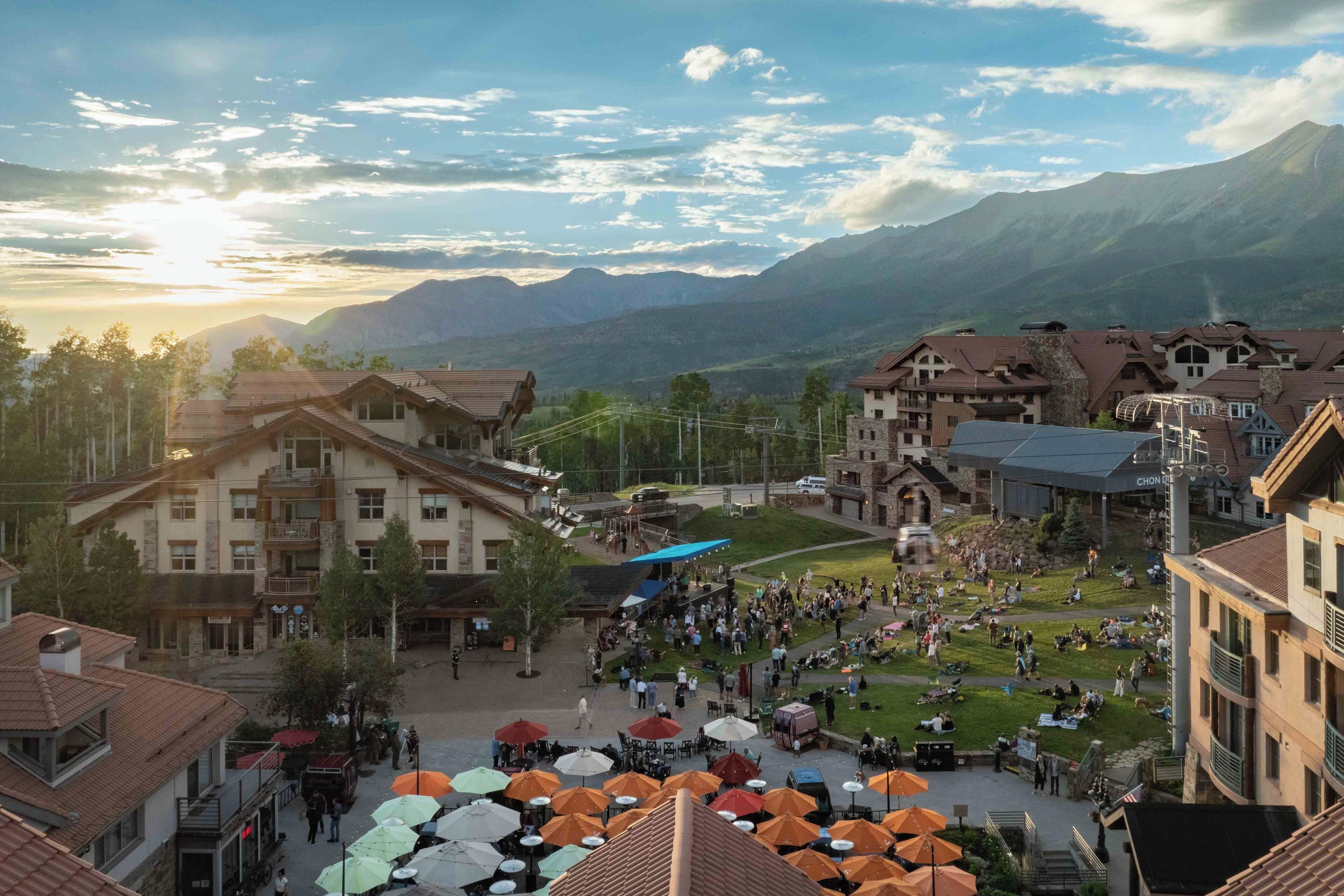 Eine bergige Stadt mit traditioneller Architektur, ein zentraler Platz mit Außenbestuhlung und Blick auf die Berge im Hintergrund.