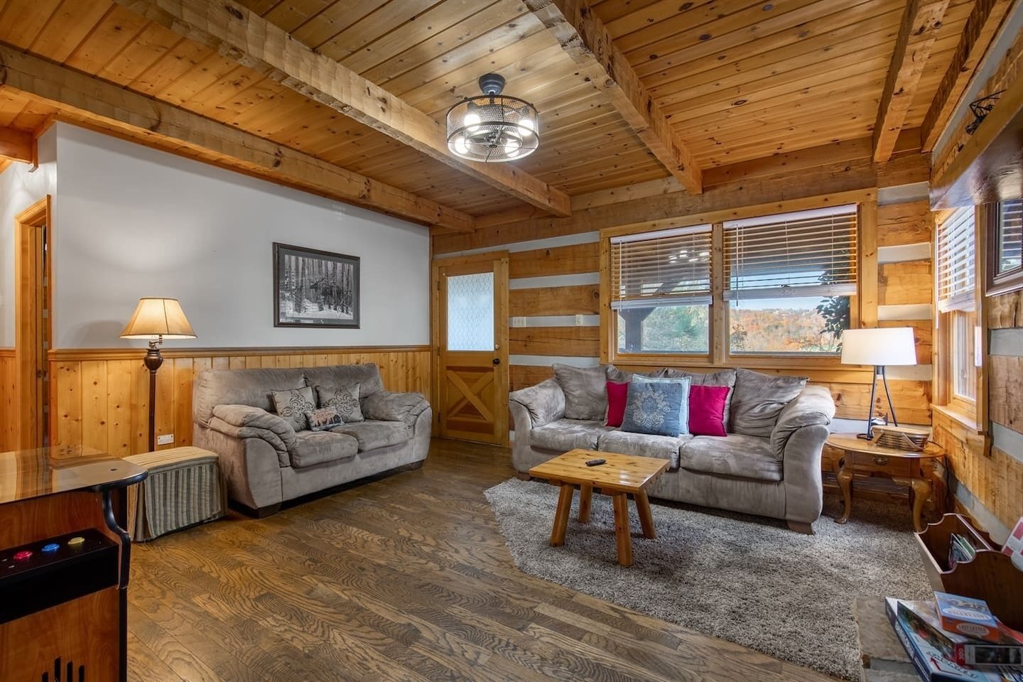 A cozy cabin interior with a wooden ceiling, two sofas, a coffee table, and a fireplace.