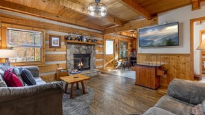 A log cabin interior with a stone fireplace, wooden walls, a couch, a coffee table, and a painting on the wall. - 1mi From Parkway ~ Hot Tub ~ Fire Place (Gatlinburg)