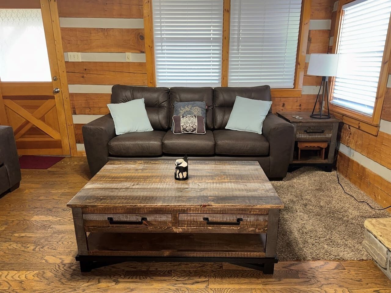 A rustic wooden room with a sofa, a coffee table, and a lamp.