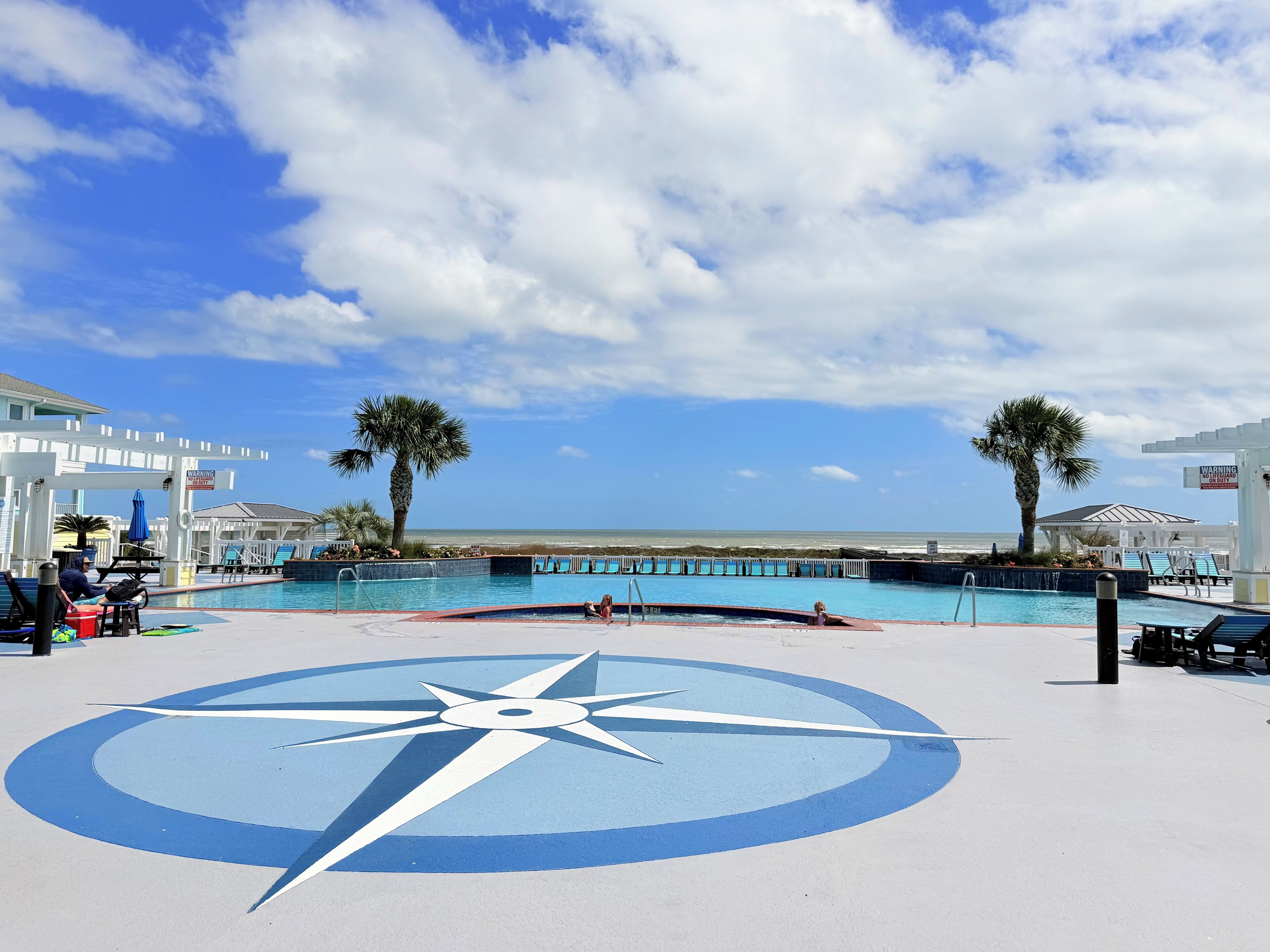 A pool area with a large compass design, palm trees, and a view of the ocean.