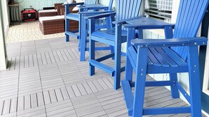 Eine überdachte Veranda mit blauen Adirondack-Stühlen, einem Ventilator und einem Ziegelpflanzgefäß.