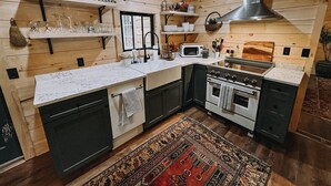 A kitchen with wooden walls, a stove, oven, microwave, and various kitchen items on shelves. - Cozy Waterfront Lake Cabin - New Listing - Adirondacks - Long Lost Lodge (Malone)