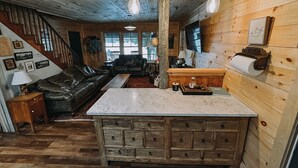 A rustic cabin interior with a wooden staircase, leather sofa, and a kitchen area with a marble countertop. - Cozy Waterfront Lake Cabin - New Listing - Adirondacks - Long Lost Lodge (Malone)