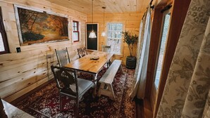 A wooden interior with a large painting, a dining table with chairs, a bench, and a patterned rug. - Cozy Waterfront Lake Cabin - New Listing - Adirondacks - Long Lost Lodge (Malone)