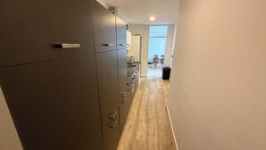 A narrow hallway with a wooden floor leading to a kitchen area with modern appliances.