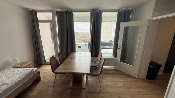 A compact room with a wooden table and chairs, a bed, and a door leading outside.