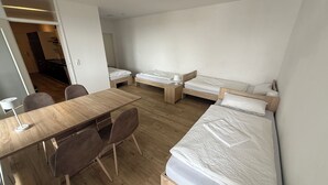 A modern, minimalistic room with a wooden floor, a wooden desk with two chairs, and two single beds with wooden frames and white bedding.